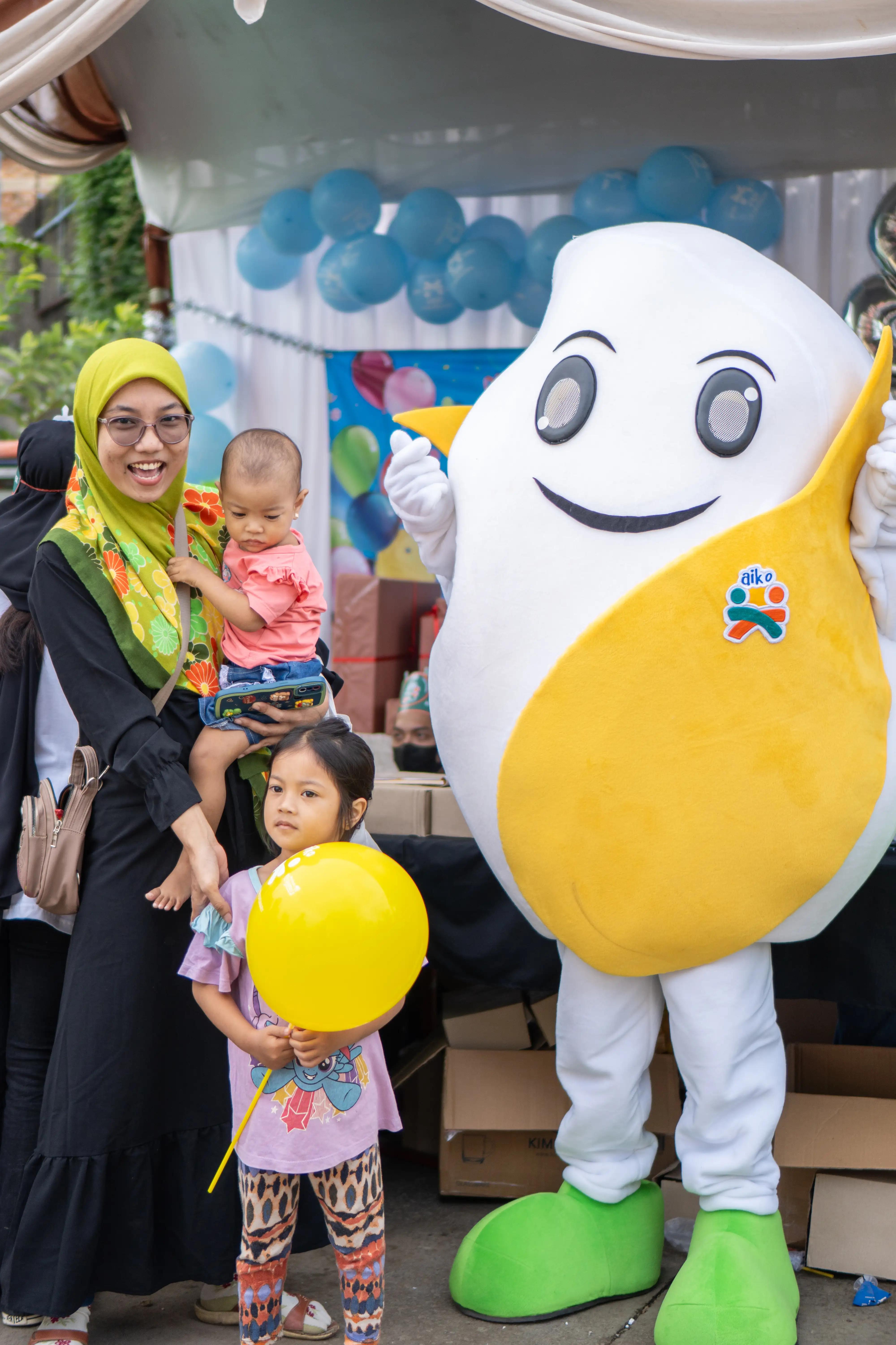Keluarga berfoto bersama maskot Aiko dalam kegiatan outlet.