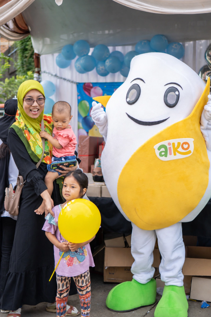 Keluarga bersama maskot AIKO berlogo terbaru dalam kegiatan outlet.